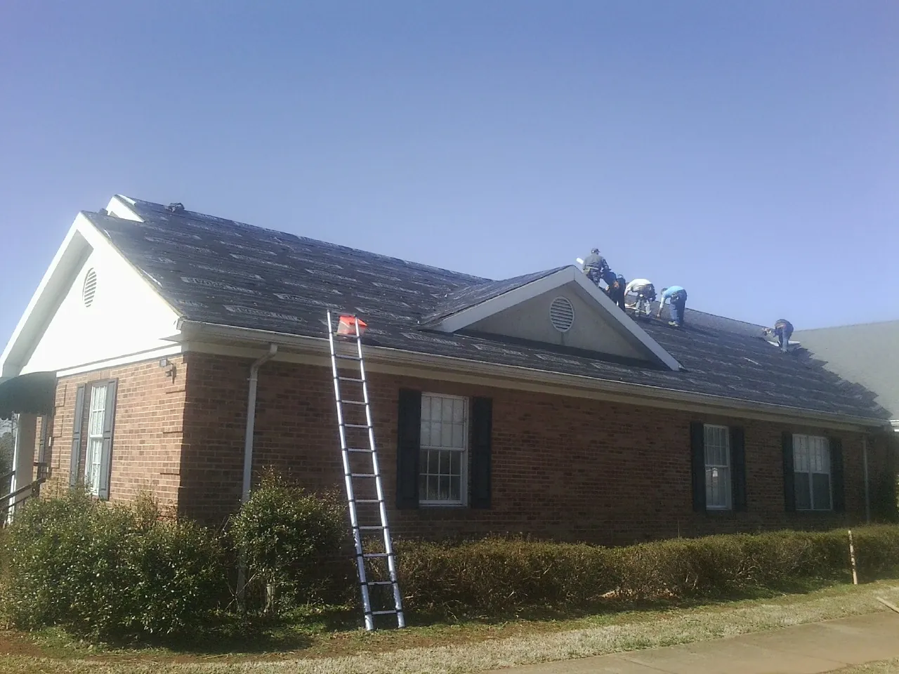 Crew tearing shingles off a brick ranch roof with a ladder set — Emergency Roof Repair work by our crew in Moultonborough