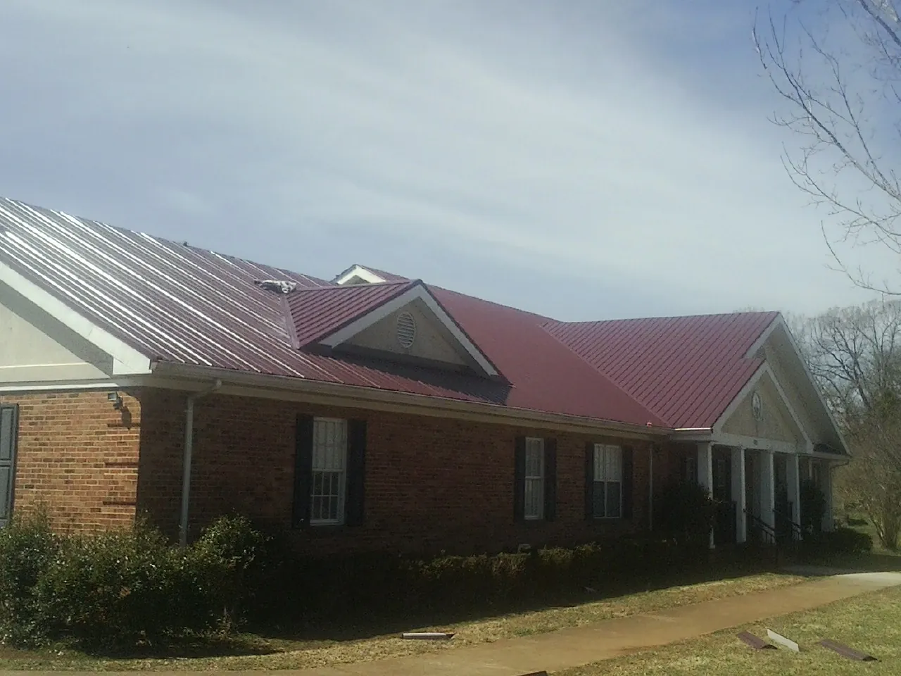 Red metal roof with gabled entries on a long brick building, from a Hail Damage Roof Repair job in Moultonborough
