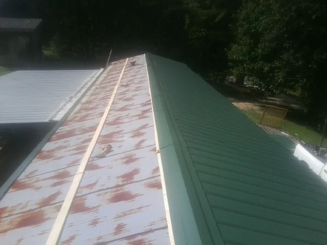 Old rusted panels beside newly installed green metal roofing — Wind Damage Roof Repair by Roofing Brothers in Moultonborough