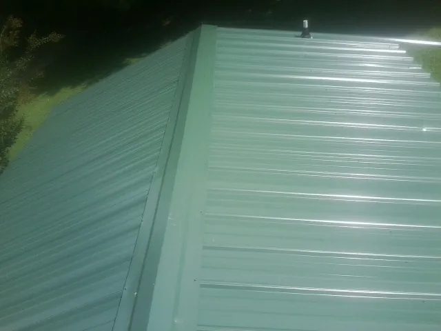 New green metal panels meeting at the ridge of a roof — Flat Roof Repair work by our crew in Moultonborough