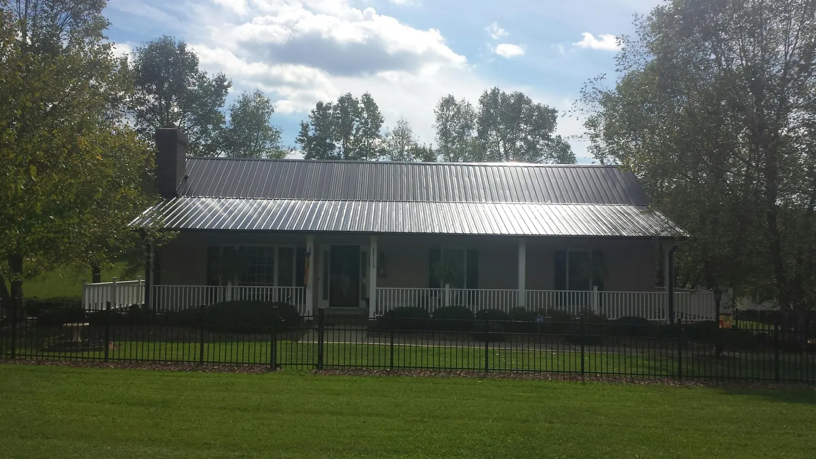 Gray metal roof on a brick ranch with a full width front porch — Gutter Guard Installation work by our crew in Moultonborough