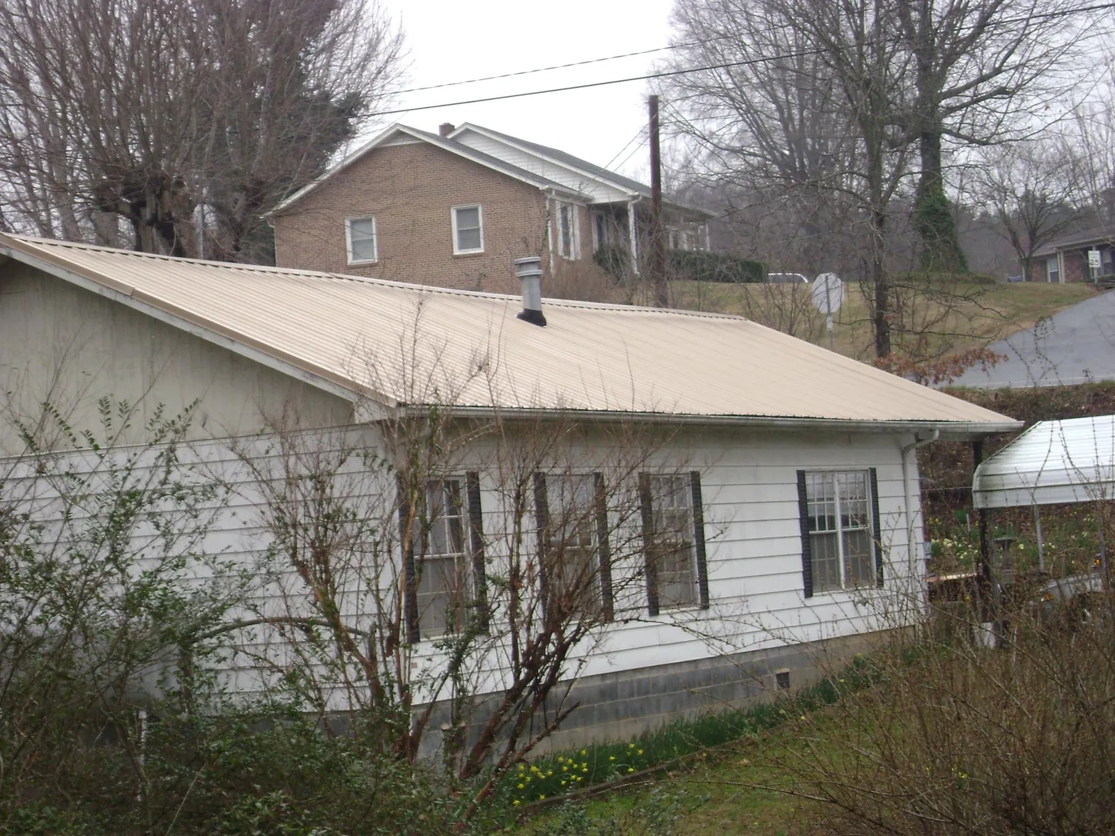Tan metal roof on a white sided house set into a hillside — Commercial Roofing by Roofing Brothers in Moultonborough