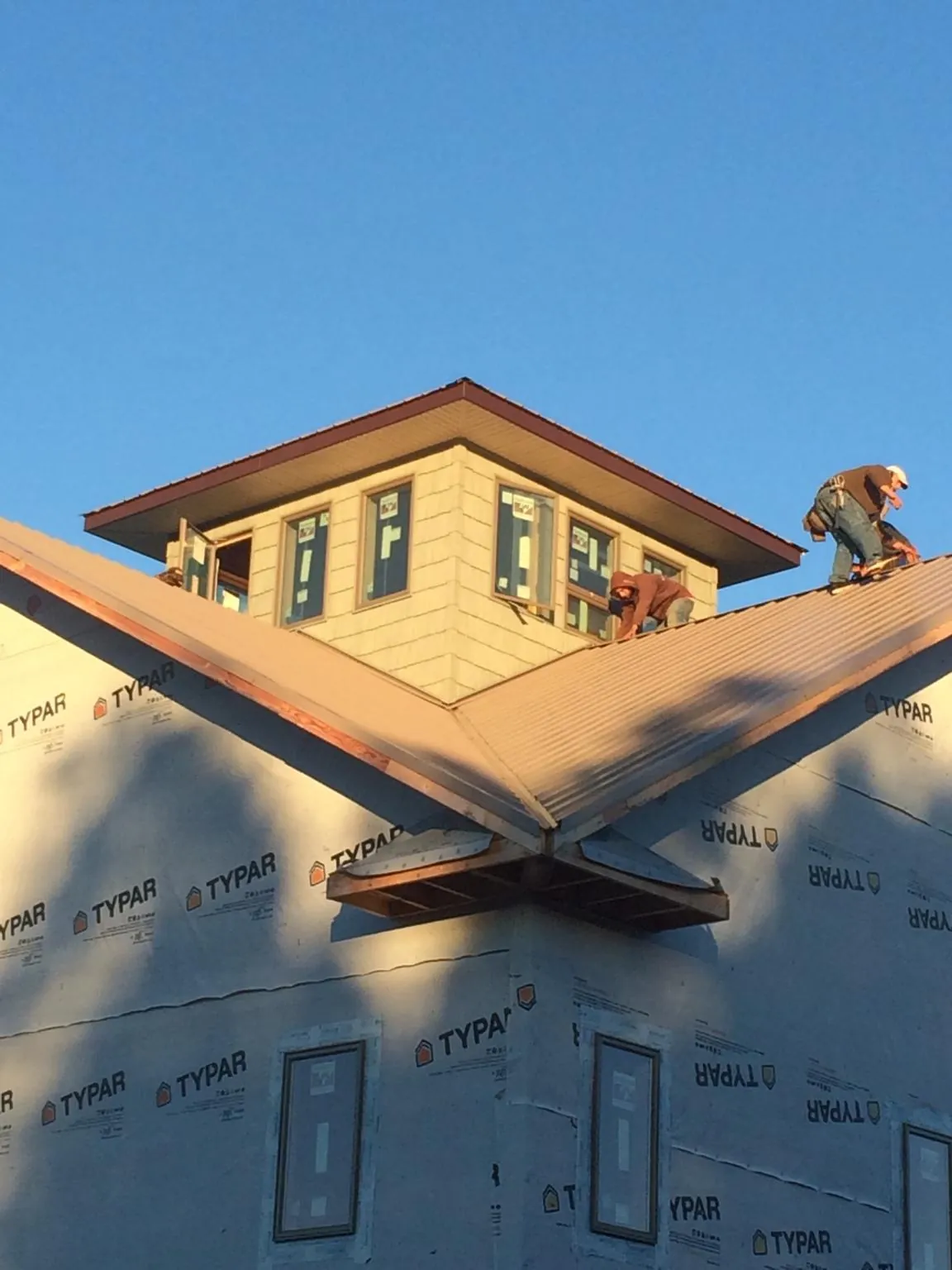 Roofers working around a rooftop cupola on a new metal roof at sunset in Moultonborough